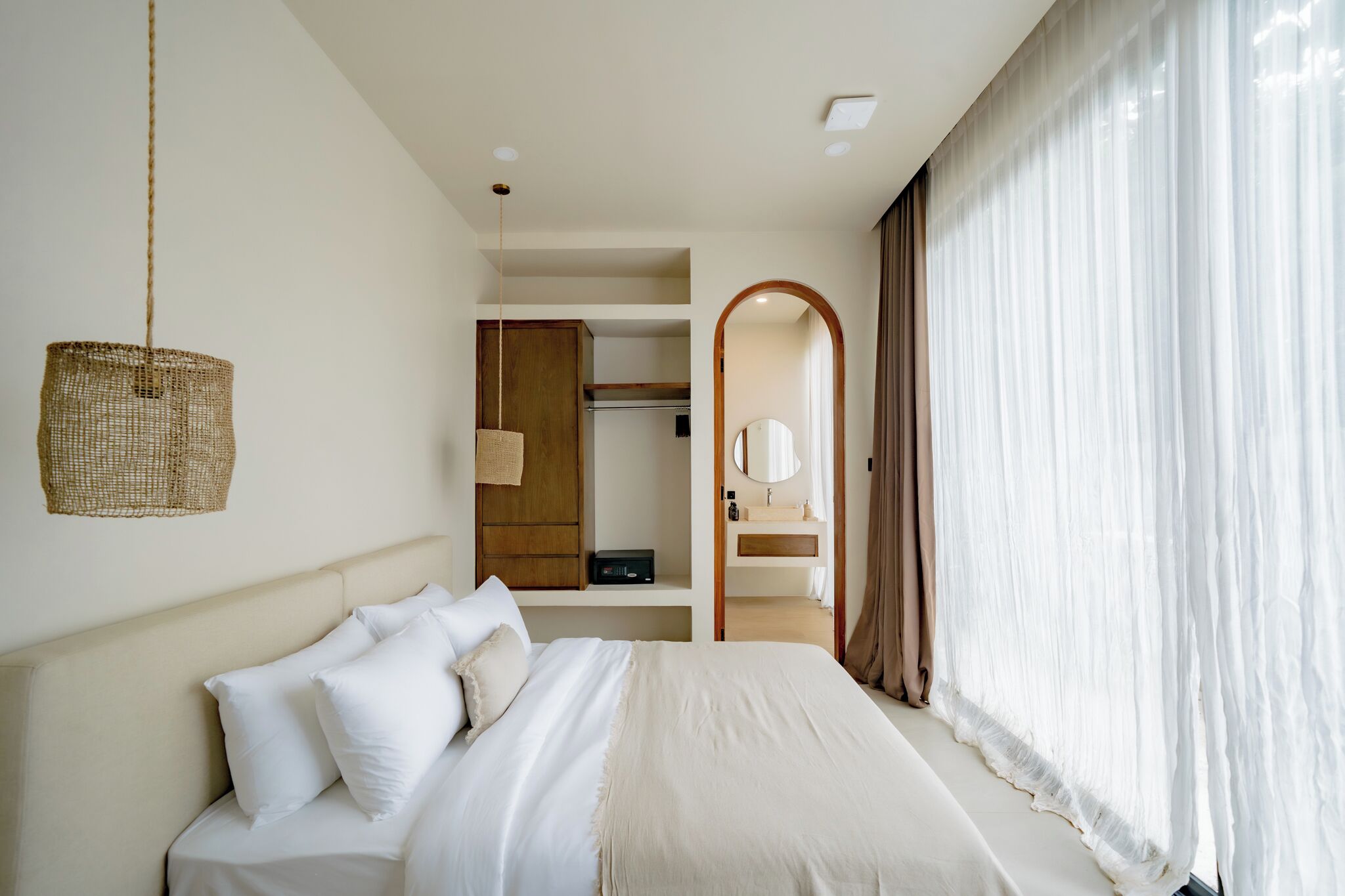 Un dormitorio con cama, una lámpara colgante, un armario y un baño visible a través de un arco.