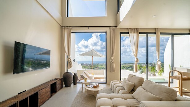 A spacious living room with a large flat-screen TV, a sofa, a coffee table, and a view of the sea through large windows. - Villa Vista al Mar (Uluwatu)