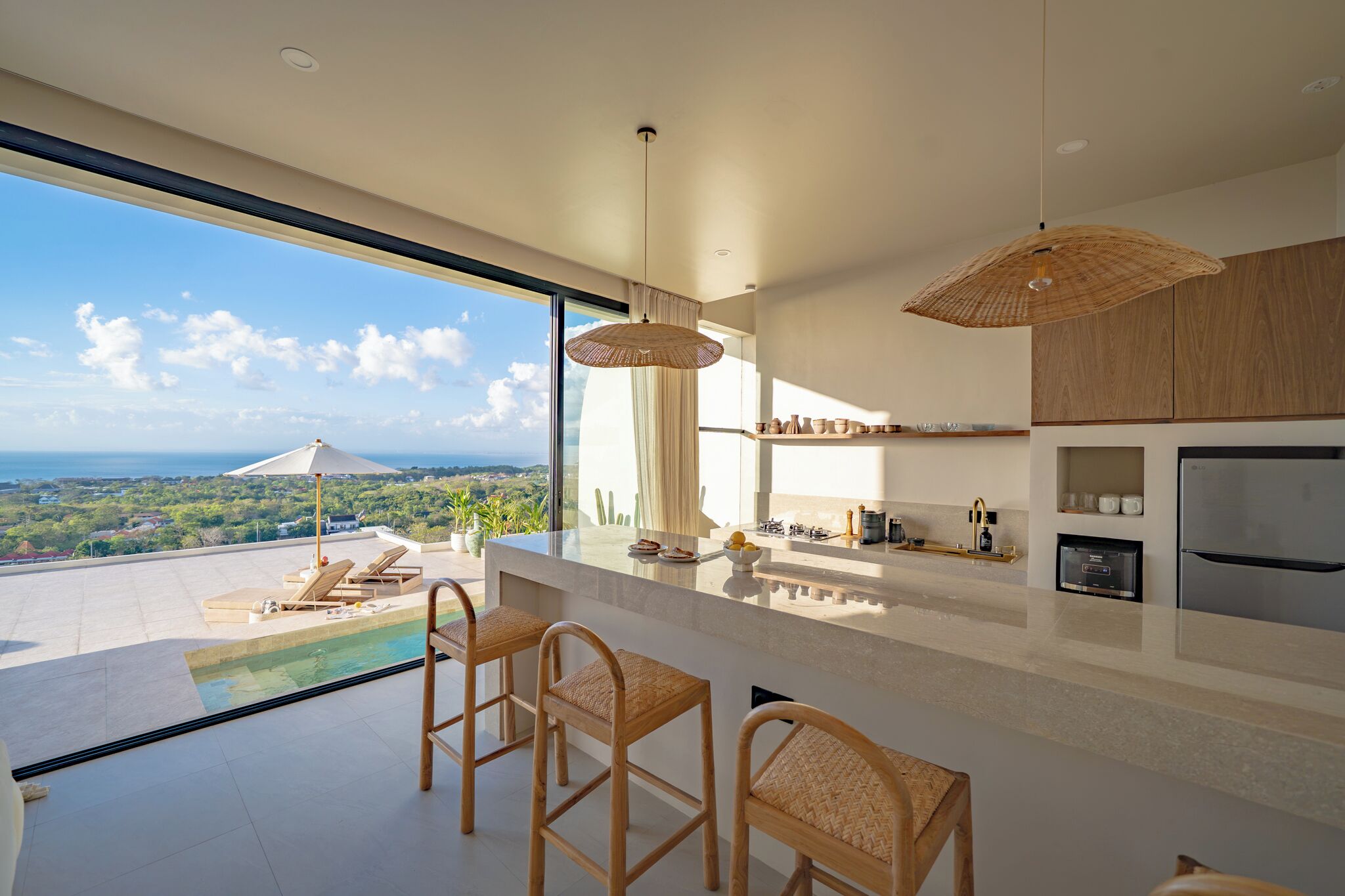 A modern kitchen with a large island, bar stools, a view of the ocean, and a pool area.