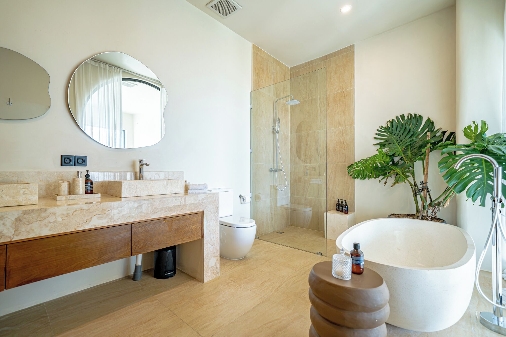 Un baño moderno con tocador de mármol, bañera independiente, ducha con mampara de vidrio y una planta en maceta.