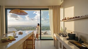 A modern kitchen with a large island, a dining area, and a view of a pool and landscape. - Villa Vista al Mar (Uluwatu)