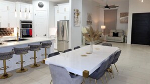 A modern kitchen with white cabinets, stainless steel appliances, and a central island with bar stools. - 3-bedroom house (Alton)