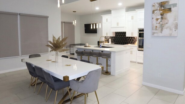 A modern kitchen with white cabinets, a central island with bar stools, and a dining area with a white table and chairs. - 3-bedroom house (Alton)