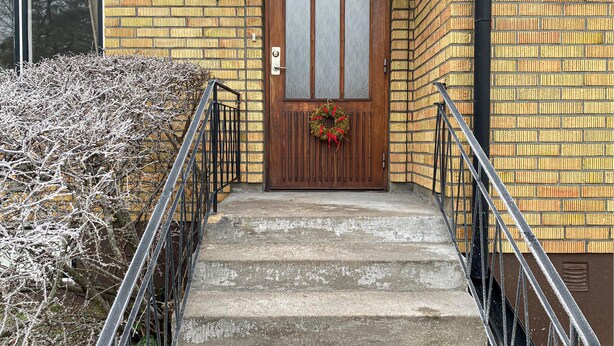 A wooden front door with a glass panel and a wreath, leading to a concrete staircase with metal railings. - 3 bedroom beautiful home in Borgholm (Borgholm)