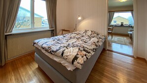 A bedroom with a bed, a desk, and a chair. There is a window with curtains, a radiator, and a door leading to another room. - 3 bedroom beautiful home in Borgholm (Borgholm)