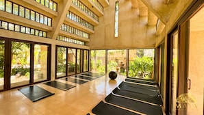 A spacious indoor area with multiple exercise mats arranged in rows, large windows allowing natural light, and a view of a lush garden. - Peregrina Tulum 116 1BR Luxury Condo (Tulum)