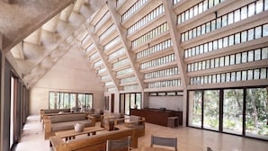 A spacious interior with high ceilings, large windows, and a modern design featuring wooden furniture and a central round table. - Peregrina Tulum 116 1BR Luxury Condo (Tulum)