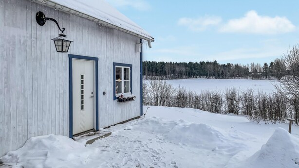 A wooden cabin with a snow-covered exterior, a front door, and a window with a hanging basket. - 1 bedroom lovely home in Söderköping (Söderköping)