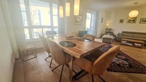Un'area pranzo con tavolo e sedie in legno, una finestra con vista e un angolo salotto con divano e tavolino.