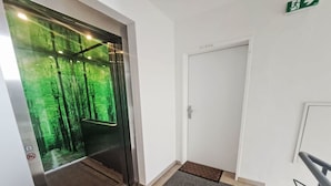 Ascensore con interni a tema forestale, una porta bianca e pavimento rivestito di moquette.