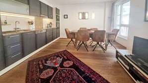 Una cucina moderna con mobili scuri, una zona pranzo con tavolo e sedie in legno e un'ampia finestra che offre luce naturale.
