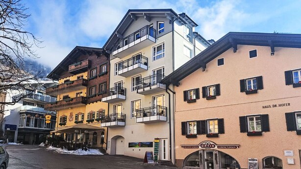 Un edificio a più piani con balconi, un cartello con la scritta 'Haus Dr. Hofer' e un negozio con insegna 'Optik'.