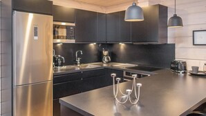 Una cocina moderna con refrigerador de acero inoxidable, gabinetes negros, una isla grande con pileta e iluminación colgante.