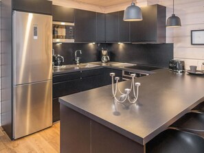 A modern kitchen with a stainless steel refrigerator, black cabinets, a large island with a sink, and pendant lighting. - Tuppuvaara by Interhome (Äkäslompolo)