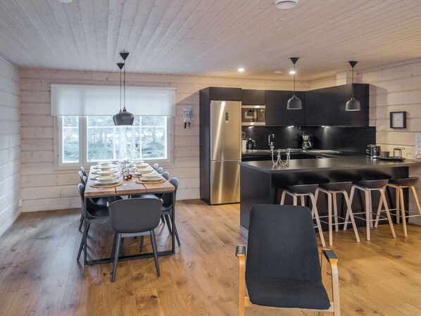 Cocina moderna con refrigerador de acero inoxidable, armarios negros y una mesa de comedor de madera para cuatro.