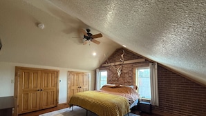 Een slaapkamer met schuine balken, een bed met een gele sprei, houten kasten en een bakstenen muur met een opgehangen dierlijk schedel.