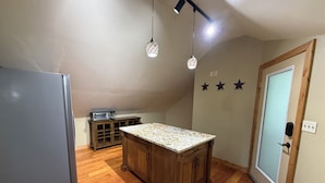 Een keuken met een houten eiland, een koelkast, een magnetron en een kast. Drie hanglampen en een deur met sterdecoratie.