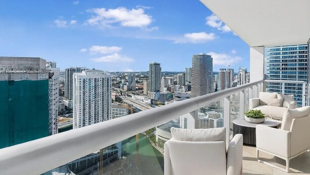A high-rise balcony with a city view, white furniture, and a glass railing. - Luxury Penthouse Brickell Water & City Views (Miami)