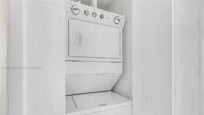 A white, compact washer and dryer unit with a control panel and a small storage compartment. - Luxury Penthouse Brickell Water & City Views (Miami)