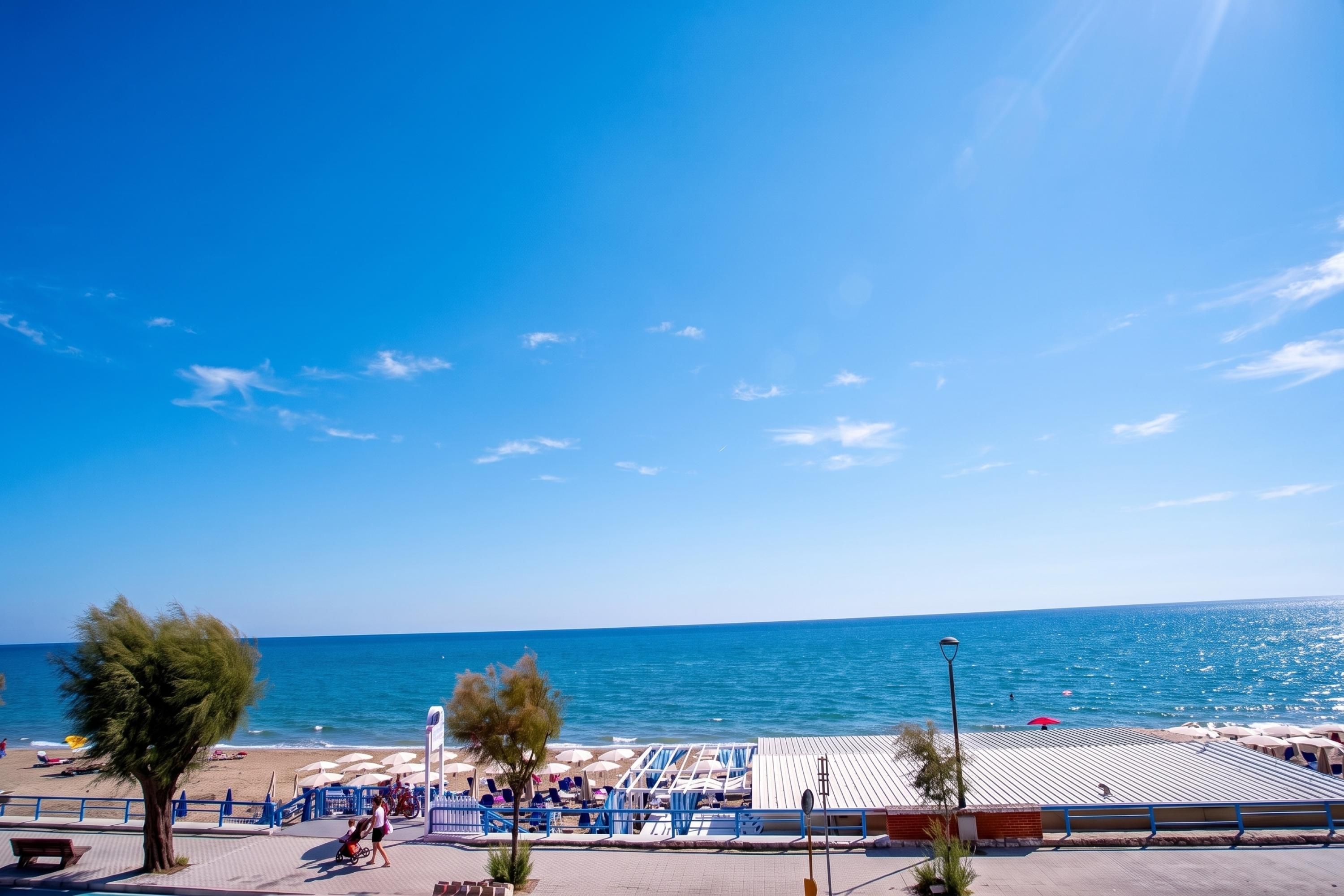 A beachside promenade with a clear view of the sea, a covered seating area, and a few trees.