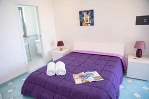 A neatly made bed with a purple bedspread, two rolled towels, and a magazine on the bed. - Villa Fortunata - Small Apartment Left, Terracina, Italy (Terracina)
