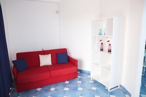 A red sofa with two pillows, a white shelving unit with decorative items, and blue patterned flooring. - Villa Fortunata - Small Apartment Right, Terracina, Italy (Terracina)