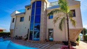 Une maison moderne à deux étages, dotée d’une piscine, de grandes fenêtres et d’un palmier.