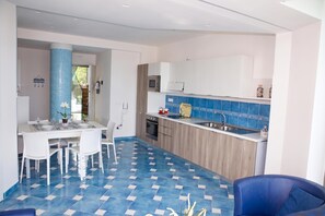 A modern kitchen with a blue tiled backsplash, a dining area with a white table and chairs, and a blue sofa. - Villa Fortunata - Small Apartment Right, Terracina, Italy (Terracina)