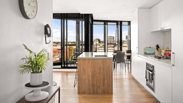 Een moderne keuken met een centraal kookeiland, grote ramen en uitzicht op de stad.