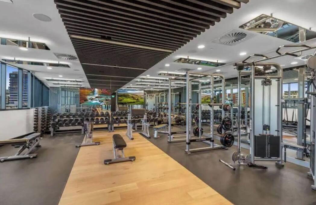 A modern gym with various weightlifting equipment, benches, and dumbbells.