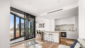 Een modern appartement met een grote schuifpui, een keuken met witte kastjes, een eetgedeelte met barkrukken en een woonkamer met een bank en salontafel.