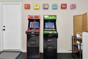 Two arcade machines, a white door, and a shelf with items.
