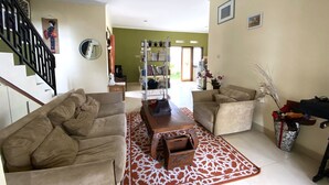 A living room with two sofas, a coffee table, and a patterned rug. There is a bookshelf, a mirror, and a staircase. - Home Sweet Home Dekat UMY by Simply Homy (Sleman)