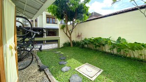 A residential area with a bicycle parked under a covered structure, a small garden with a lawn, and a wall with a window. - Home Sweet Home Dekat UMY by Simply Homy (Sleman)