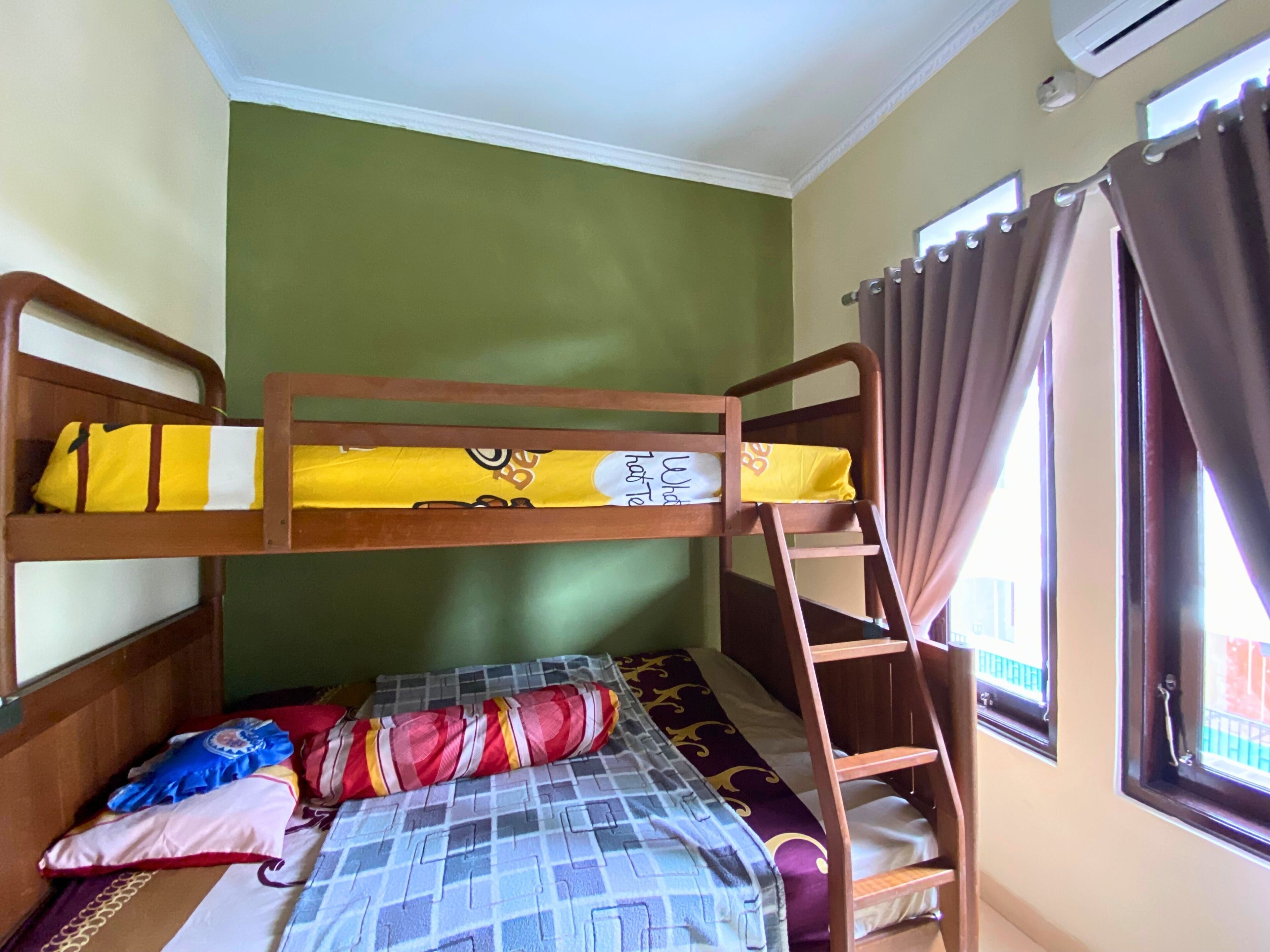 Habitación con literas, una escalera, una ventana con cortinas y una cama con manta estampada.