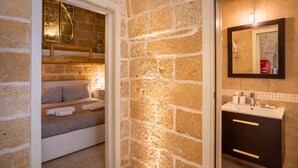 Ein Schlafzimmer mit Steinwand, einem hölzernen Bett und einem Nachttisch mit Lampe.