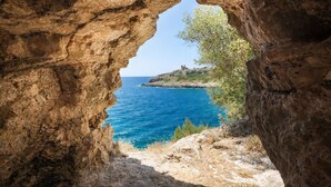 Eine natürliche Felsformation mit Blick auf das Meer und eine entfernte Hügelkette mit einer Bebauung.