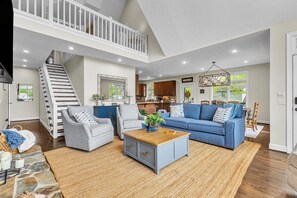A spacious living area with a staircase, a blue sofa, a wooden coffee table, and a kitchen in the background.