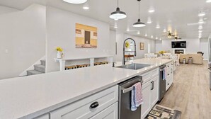 Een moderne keuken met een centraal eiland, hangende lampen en een eethoek met een bank en tafel.
