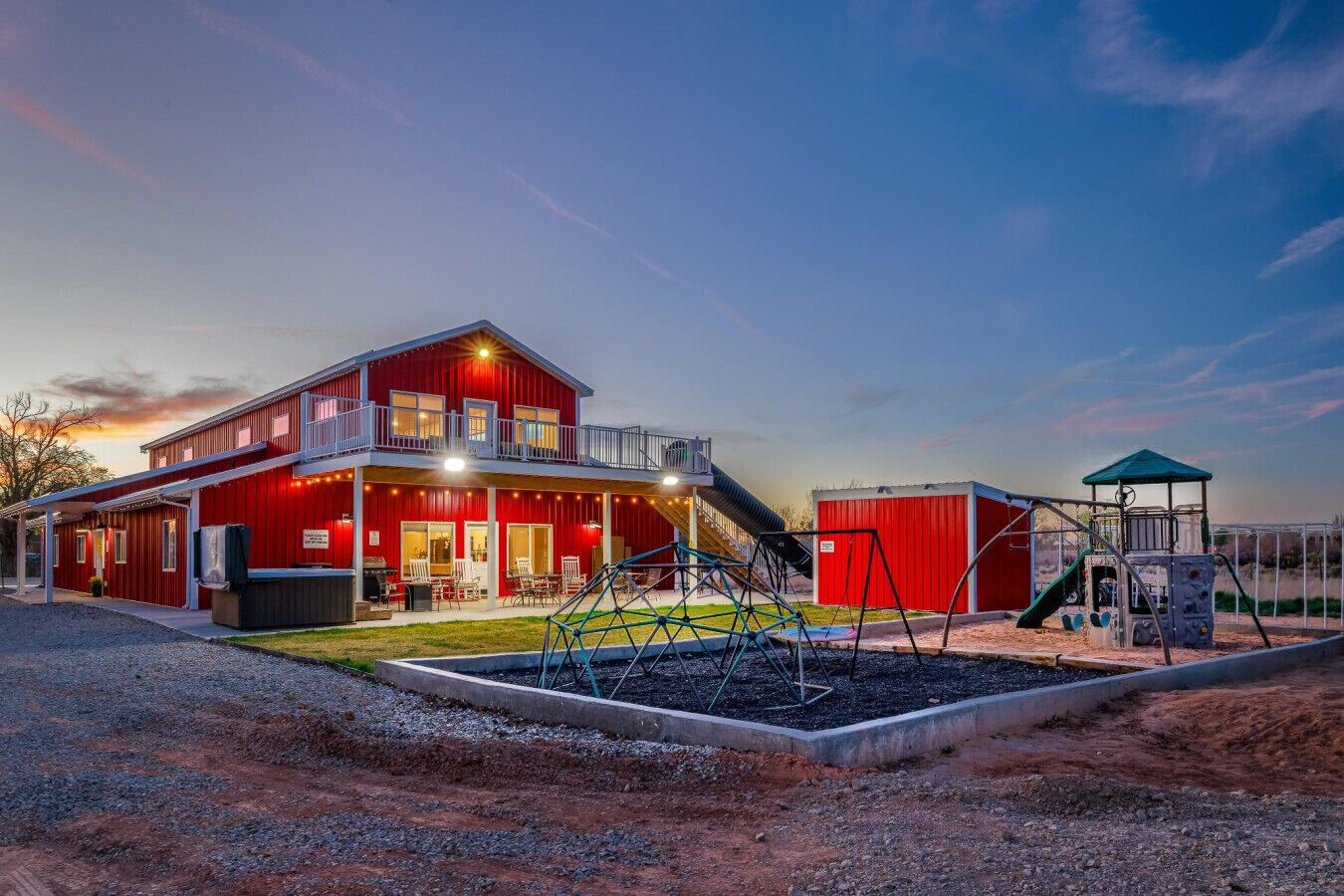 Un edificio rojo con balcón, parque infantil y zona cubierta.