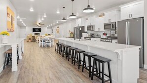 Uma cozinha moderna com armários brancos, eletrodomésticos de aço inoxidável e banquetas pretas.