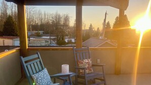 Un balcón con dos mecedoras, una mesita y vista a una zona residencial al atardecer.