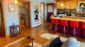 Una sala de estar acogedora con piso de madera, un sofá, una mesa de centro y una zona de cocina con barra y taburetes rojos.