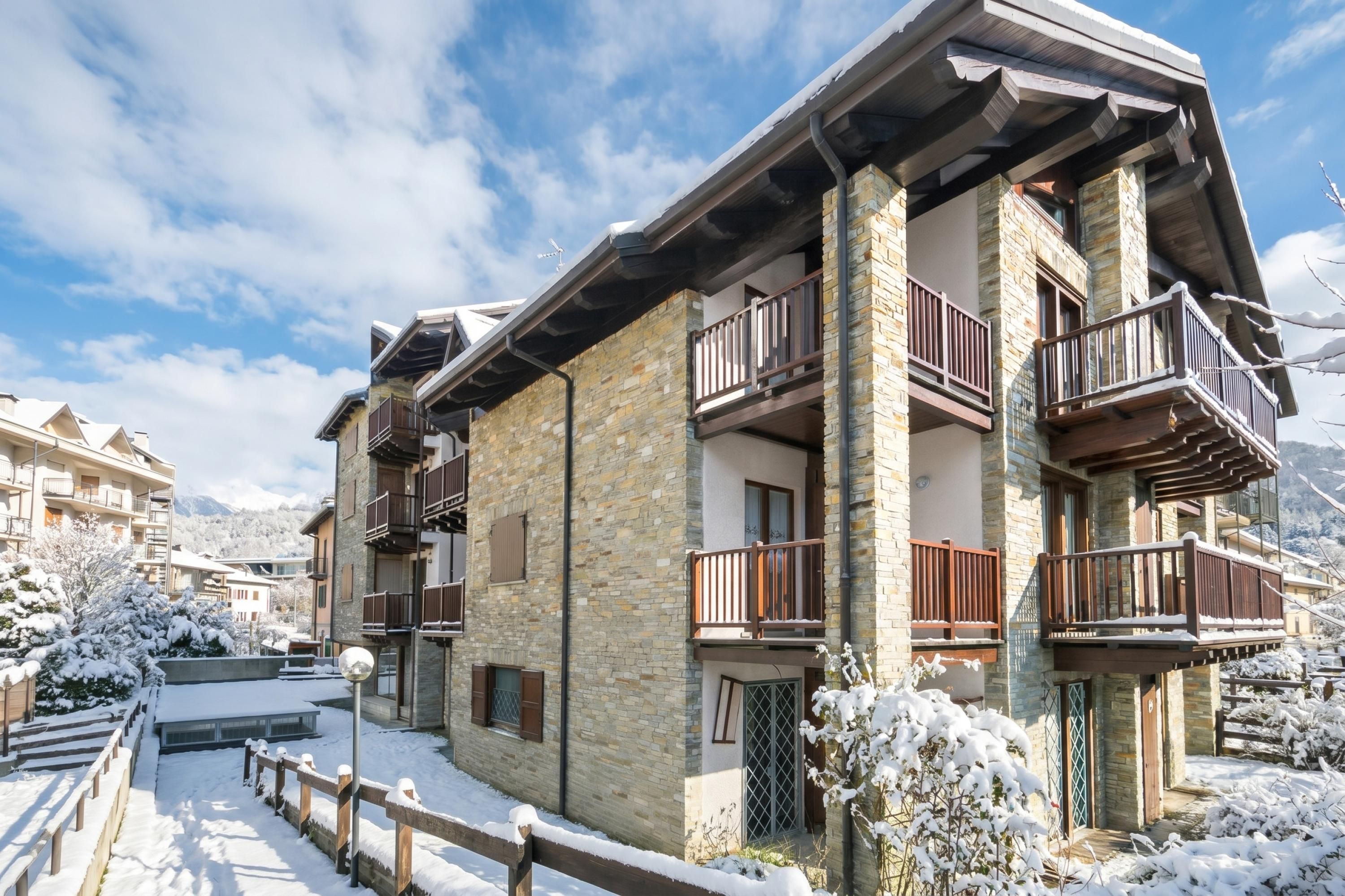 Un edificio de varios pisos con fachada de piedra y balcones, rodeado de árboles nevados y un cielo despejado.