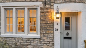 Une façade en pierre avec une fenêtre et une porte peintes en blanc, le numéro « 28 » au-dessus de la porte et une lanterne fixée au mur.