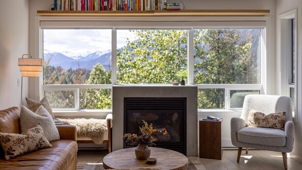 A cozy living room with a fireplace, a sofa, a chair, and a bookshelf.