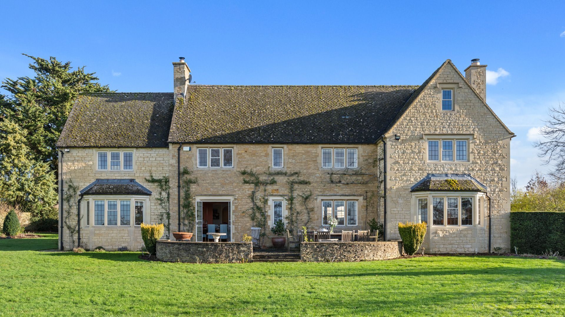 A large stone house with a well-maintained lawn, multiple windows, and a chimney.