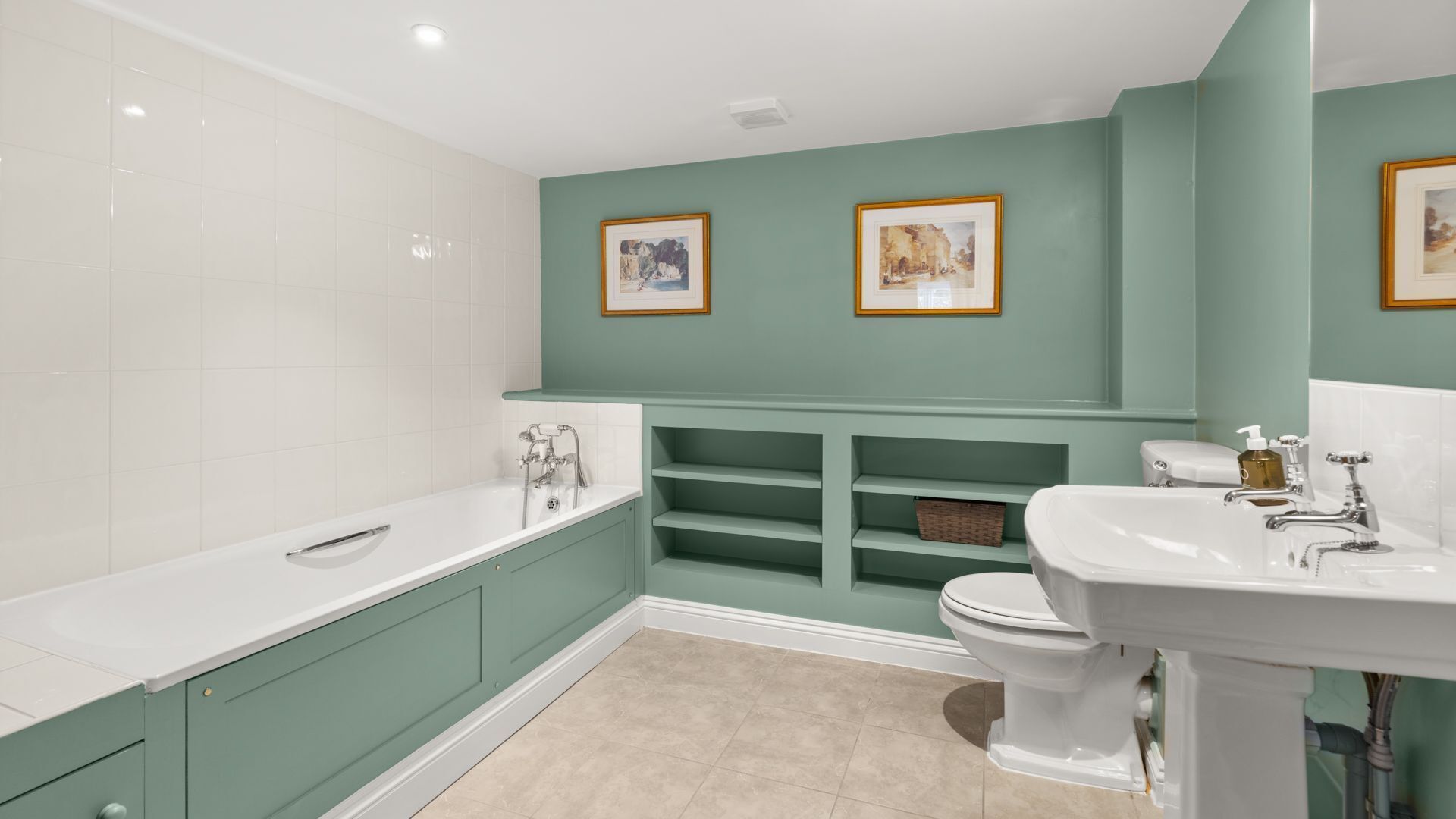 A bathroom with a bathtub, toilet, and sink, with green walls and two framed pictures.