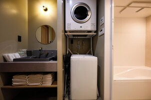 A compact hotel room with a washing machine, a sink with a mirror, and a bed.