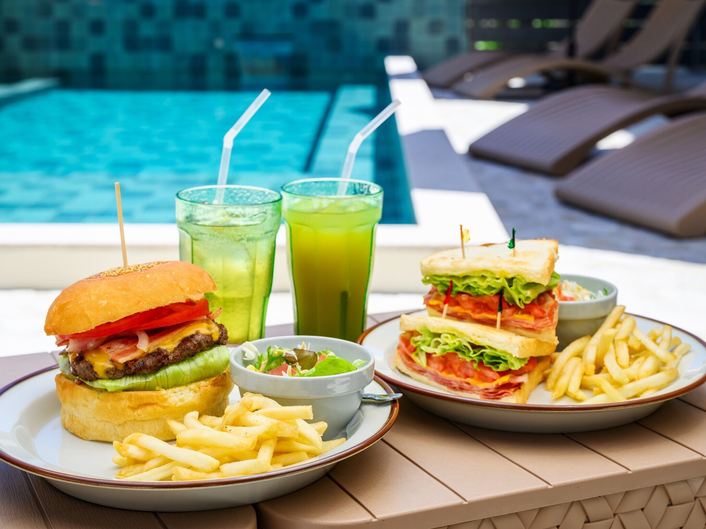 A poolside dining setup with a burger, fries, and two drinks.